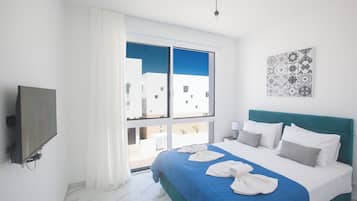 Quarto de hotel com cama, televisão, janela com cortinas e vista para edifícios.