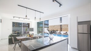 Una cocina moderna con una isla grande, un área de comedor con mesa de vidrio y vistas a una piscina.