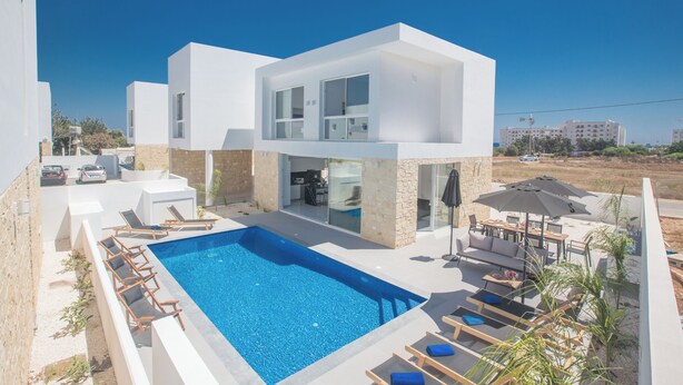 Una casa moderna de dos pisos con piscina, mobiliario exterior y vista de los alrededores.