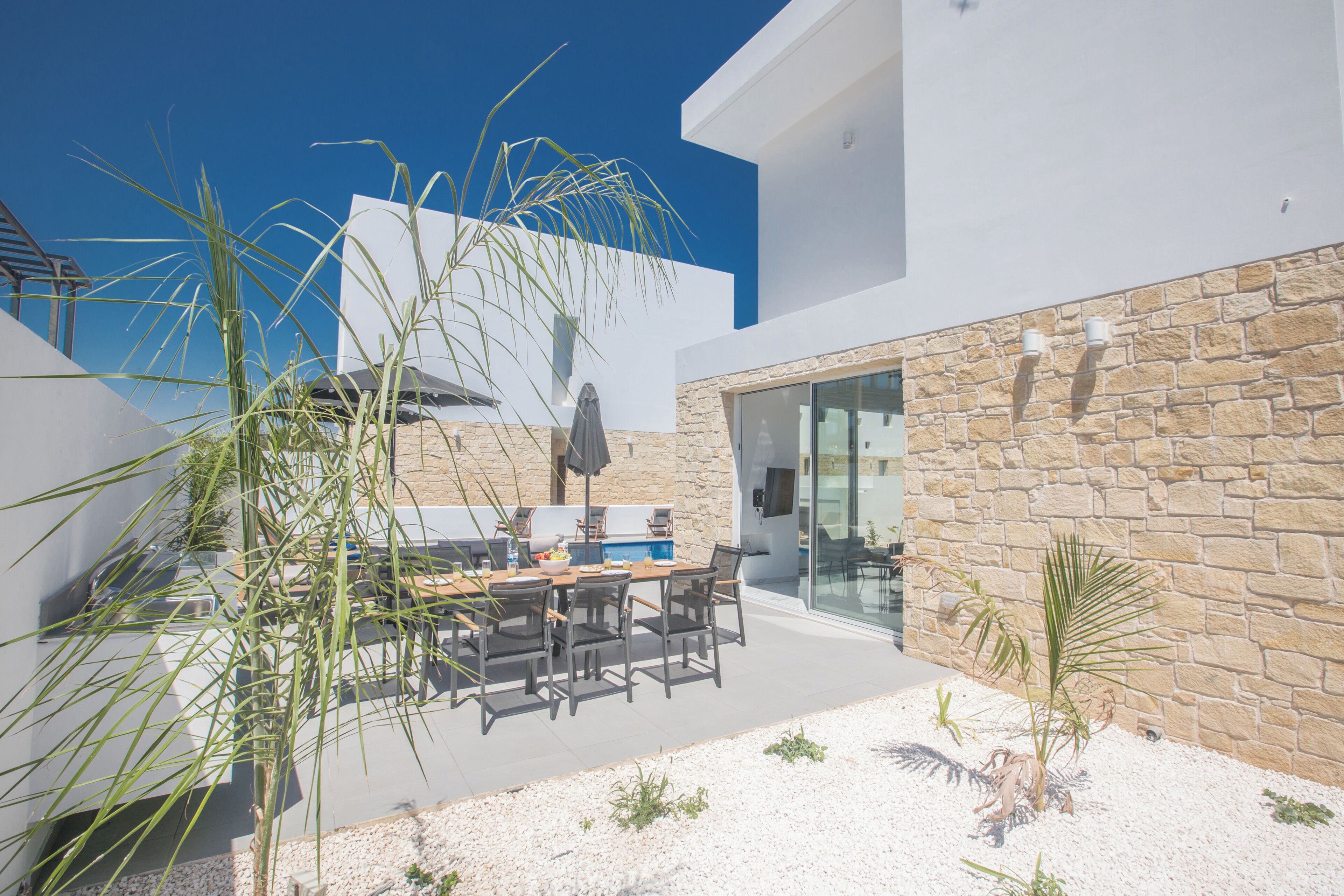 Une terrasse extérieure moderne, dotée d’une table et de chaises, entourée de plantes et d’un mur en pierre.
