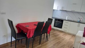 Une cuisine de taille modeste, avec des meubles blancs, une table à manger recouverte d’une nappe rouge et des chaises noires.