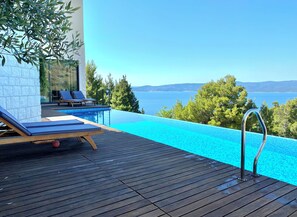 An infinity pool with a wooden deck, lounge chairs, and a view of the sea.