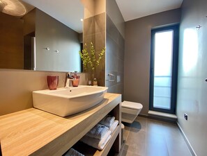 A modern bathroom with a large sink, mirror, and a toilet.