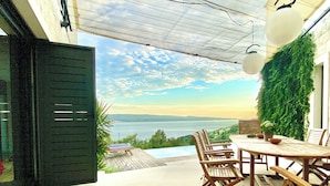 Un patio al aire libre con una mesa y sillas, vista al mar y una pared verde.