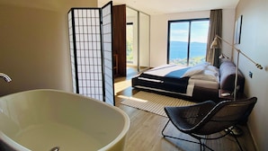 Un dormitorio moderno con una bañera grande, una cama con vistas y una puerta corredera que da a un balcón.