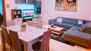 A living room with a TV, sofa, dining table, chairs, and decorative items.
