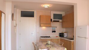 A compact kitchen with wooden cabinets, a gas stove, a microwave, and a refrigerator. - Beach Front Apartment With sea View (San Michele al Tagliamento)