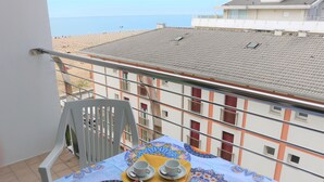 A balcony with a table set for two, a chair, and a view of the sea. - Beach Front Apartment With sea View (San Michele al Tagliamento)
