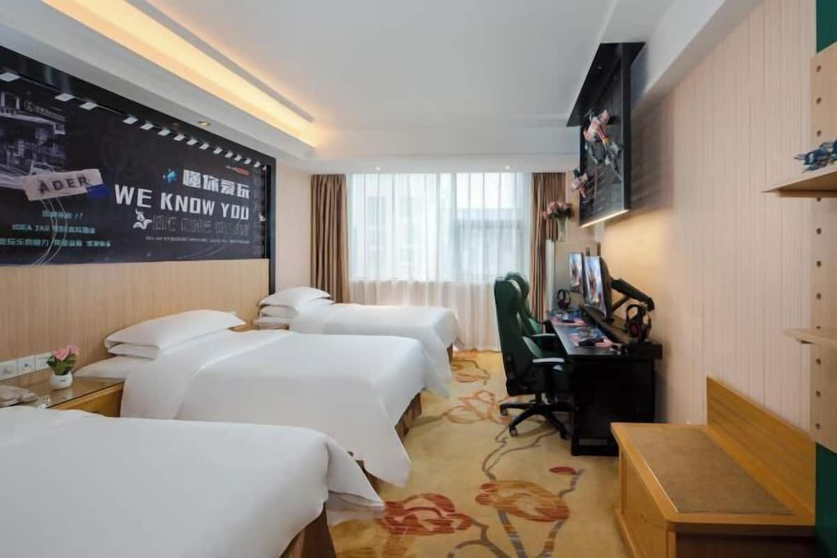 Une chambre d’hôtel avec trois lits, un bureau, une chaise et une grande affiche au mur.