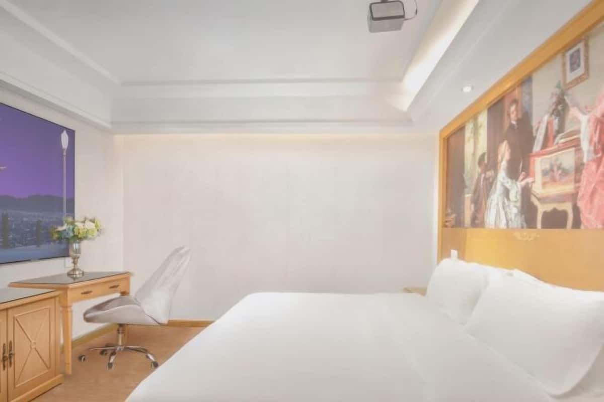 Une chambre d’hôtel avec un lit, un bureau, une chaise, une télévision et un tableau au mur.
