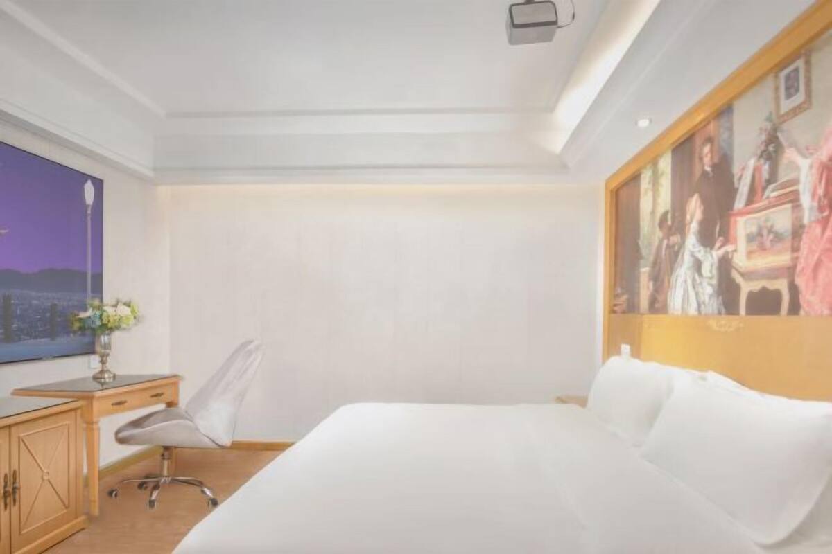 Hotellihuone, jossa on sänky, työpöytä, tuoli, televisio ja taulu seinällä.