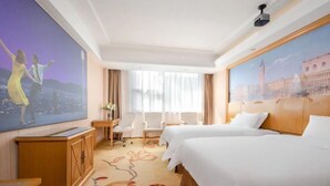 A hotel room with two beds, a desk, a chair, a TV, and a large window with curtains.