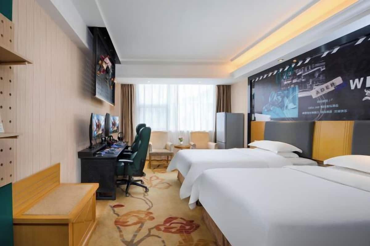 Une chambre d’hôtel avec deux lits, un bureau avec un ordinateur, une chaise, une petite table et un téléviseur fixé au mur.