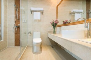 A modern bathroom with a glass-enclosed shower, a white toilet, a large mirror, and a sink with a vase of flowers.