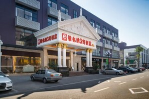 A hotel with a prominent entrance, a parking lot with several cars, and a street with buildings in the background.