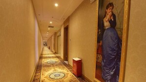 A long hallway with patterned carpet and a painting of a woman on the wall.
