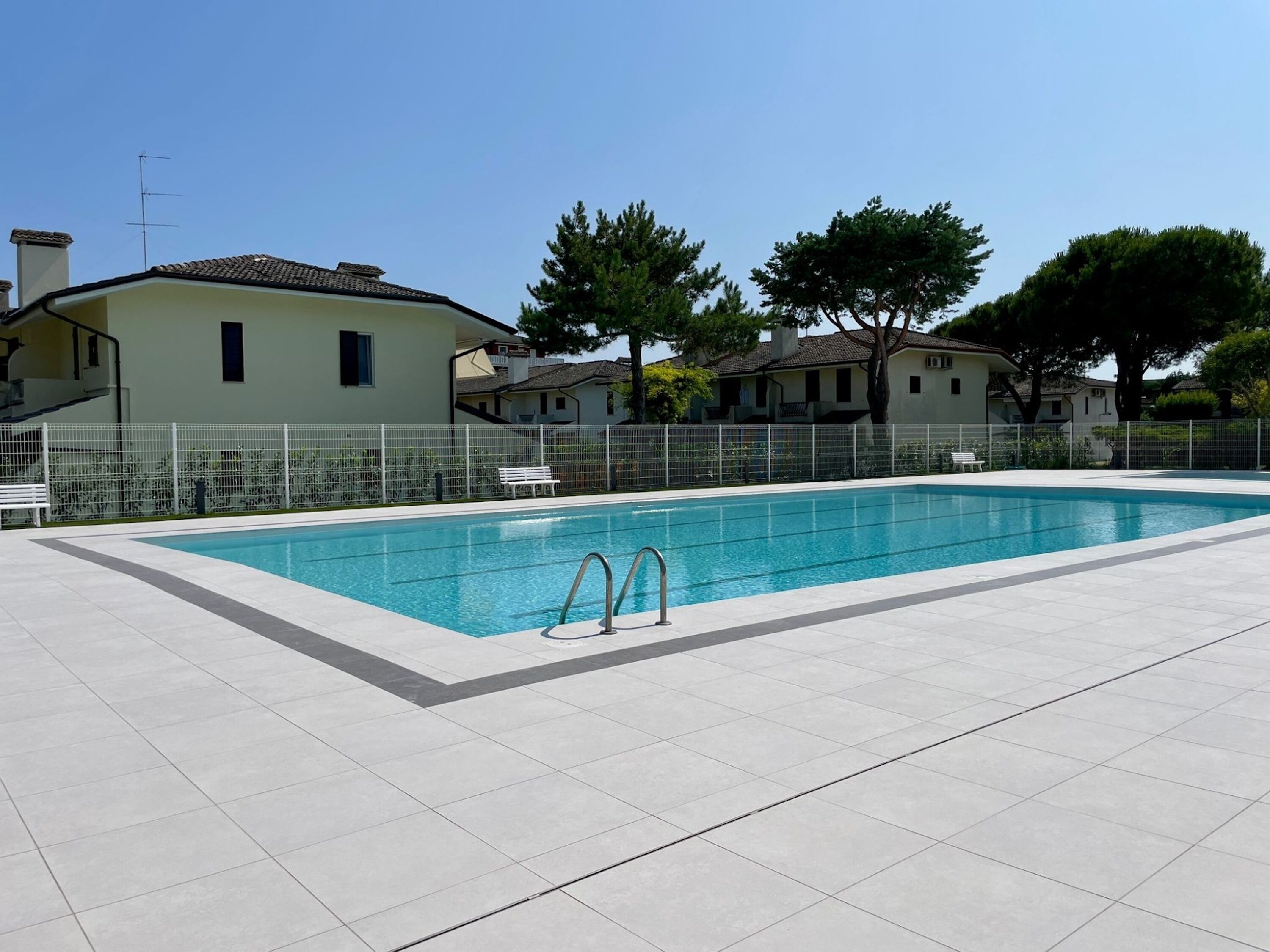 A rectangular swimming pool with a metal ladder, surrounded by a white tiled deck.