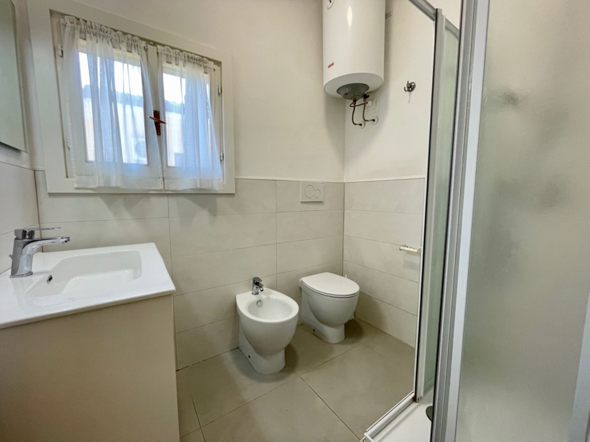 A bathroom with a sink, bidet, toilet, and a shower area.
