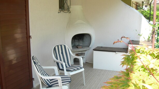 A patio area with two striped chairs, a small fireplace, and a white table. - Holiday Home With Garden and Shared Pool (Caorle)