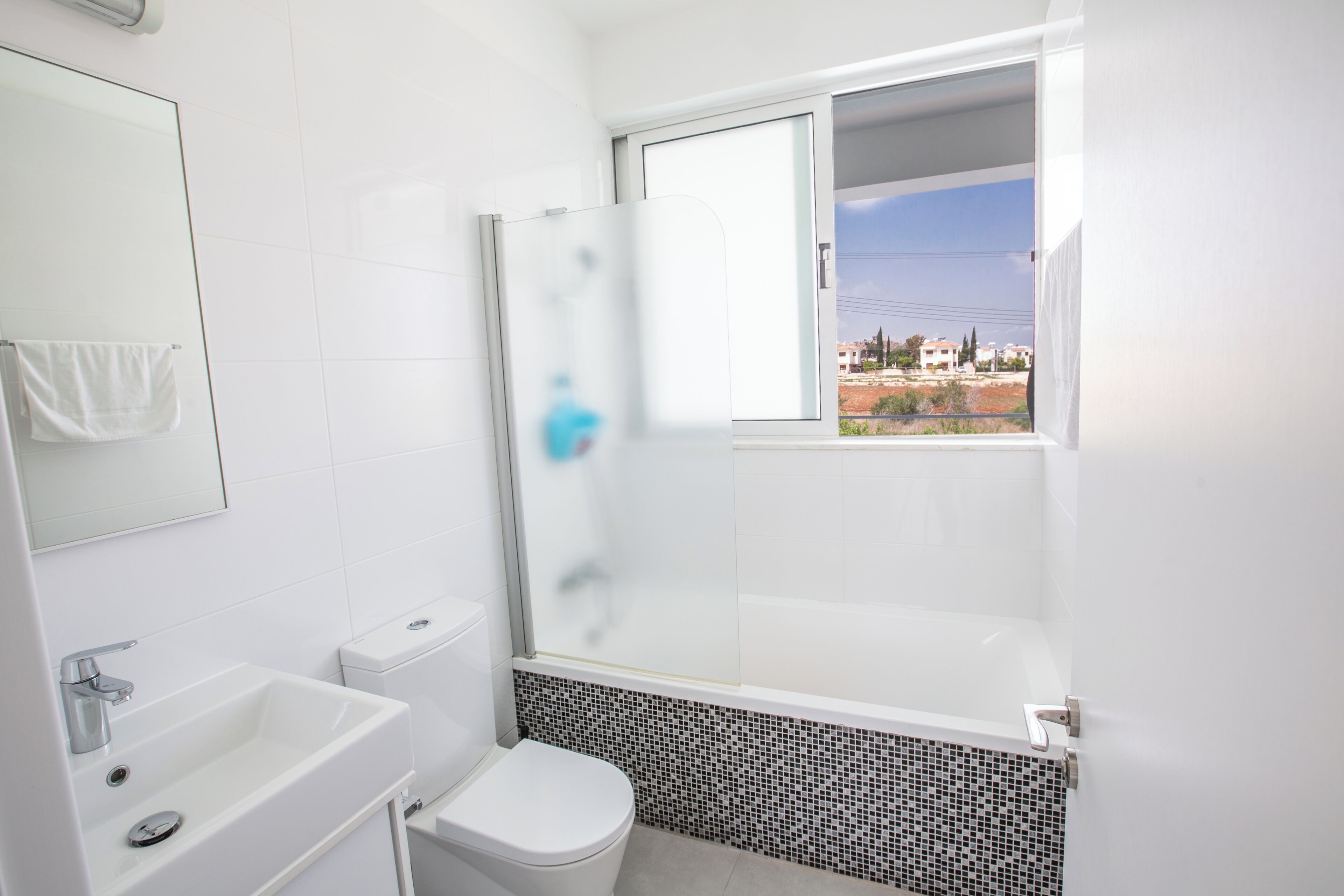 A modern bathroom with a white sink, toilet, and shower. A window provides a view of the outside.