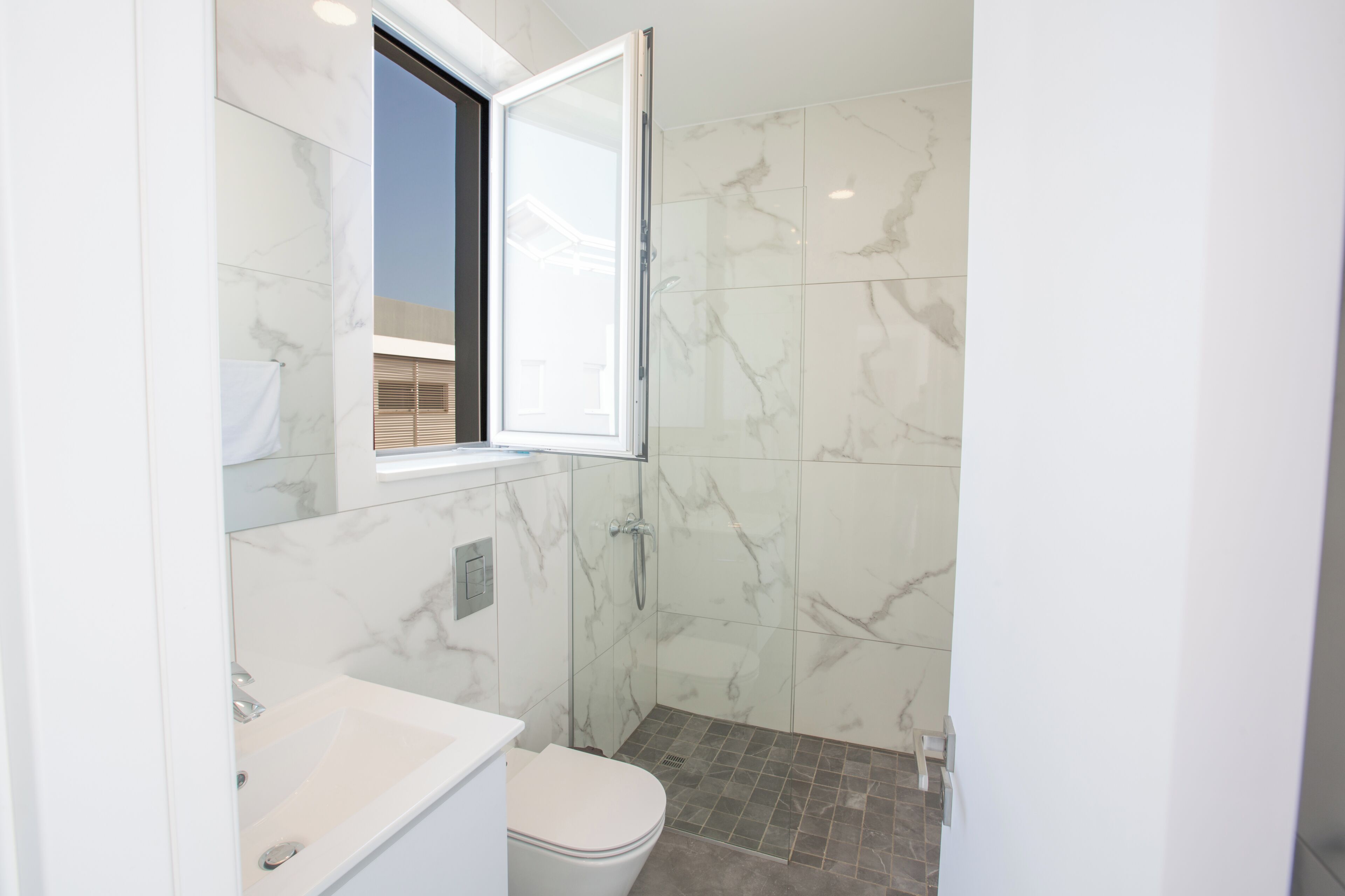 Un baño moderno con inodoro y lavamanos blancos, y una cabina de ducha de vidrio.