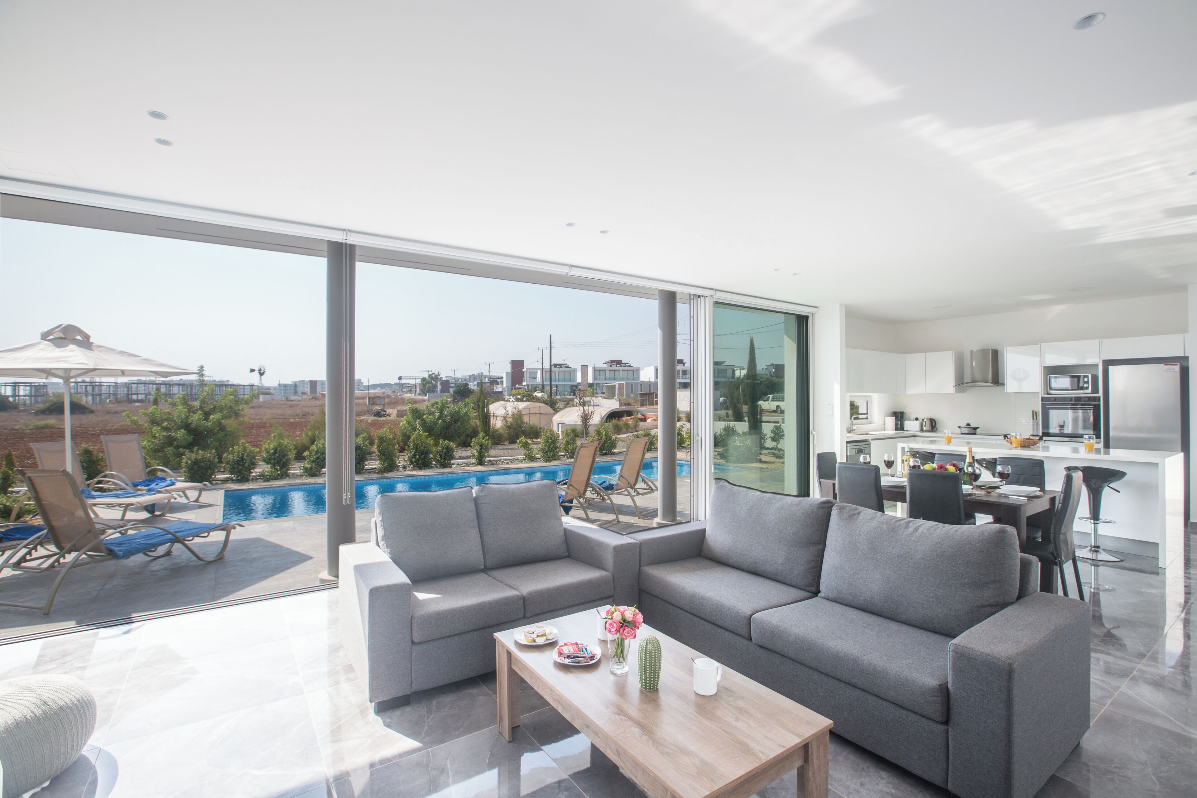 A modern living room with a gray sofa, a wooden coffee table, and a view of a swimming pool and cityscape.