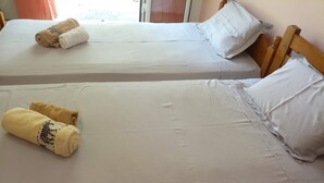 Due letti con lenzuola bianche e asciugamani arrotolati, una testiera in legno e una finestra con tende.