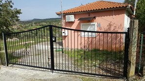 Una proprietà recintata con un edificio rosa, un cancello in metallo e vista su un paesaggio collinare.