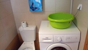 Un bagno compatto con il water, una lavatrice e un lavabo verde sopra la lavatrice.