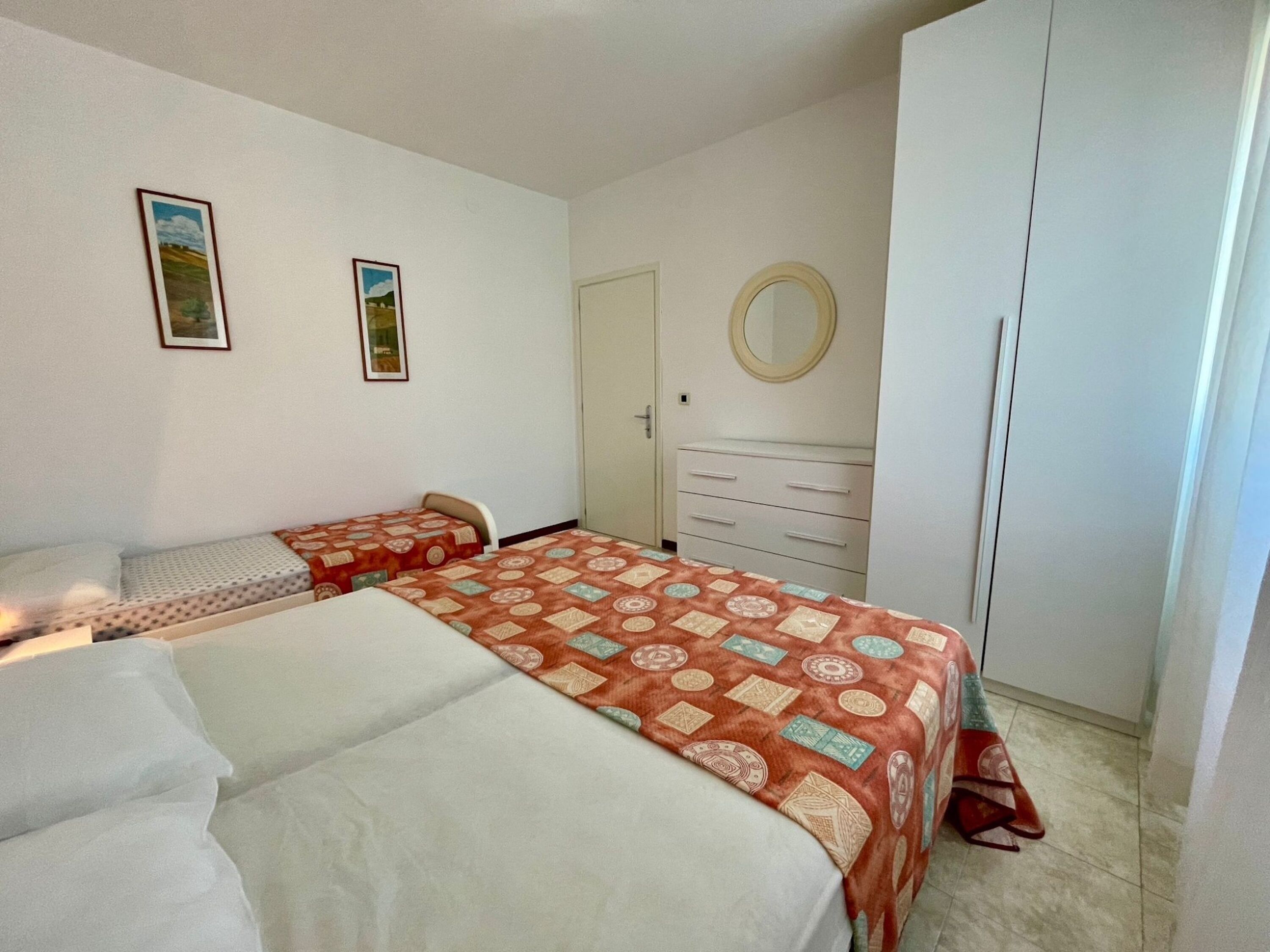 A bedroom with two beds, a dresser, a chair, and two framed pictures on the wall.