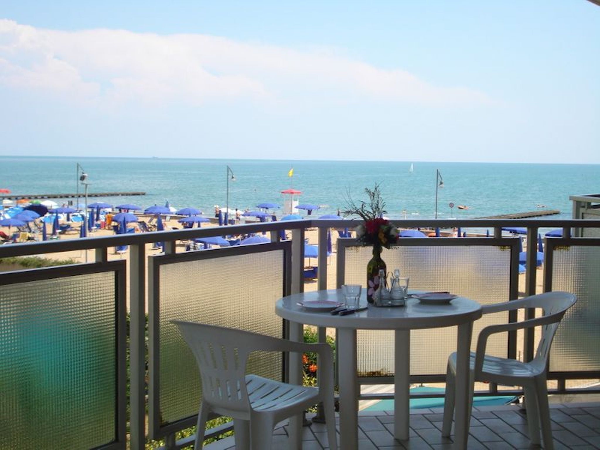 A balcony with a table and chairs overlooking a beach with umbrellas.