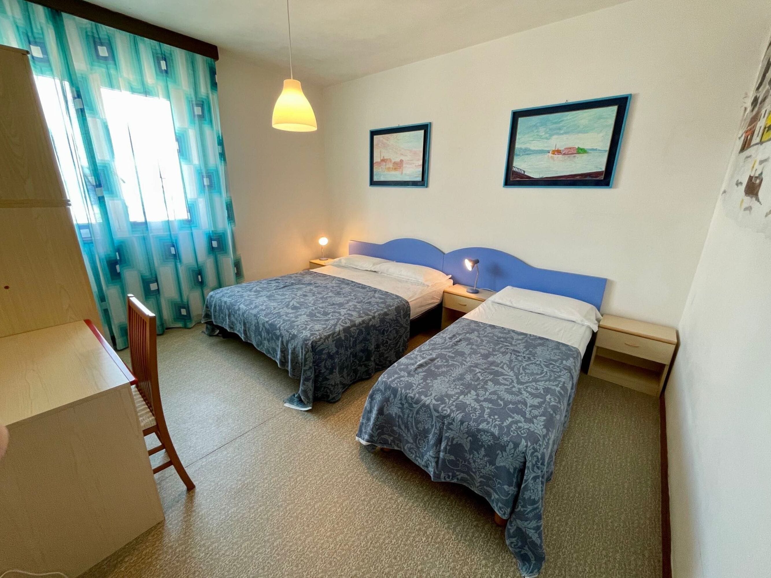 Une chambre avec deux lits simples, un bureau, une chaise et un luminaire suspendu.