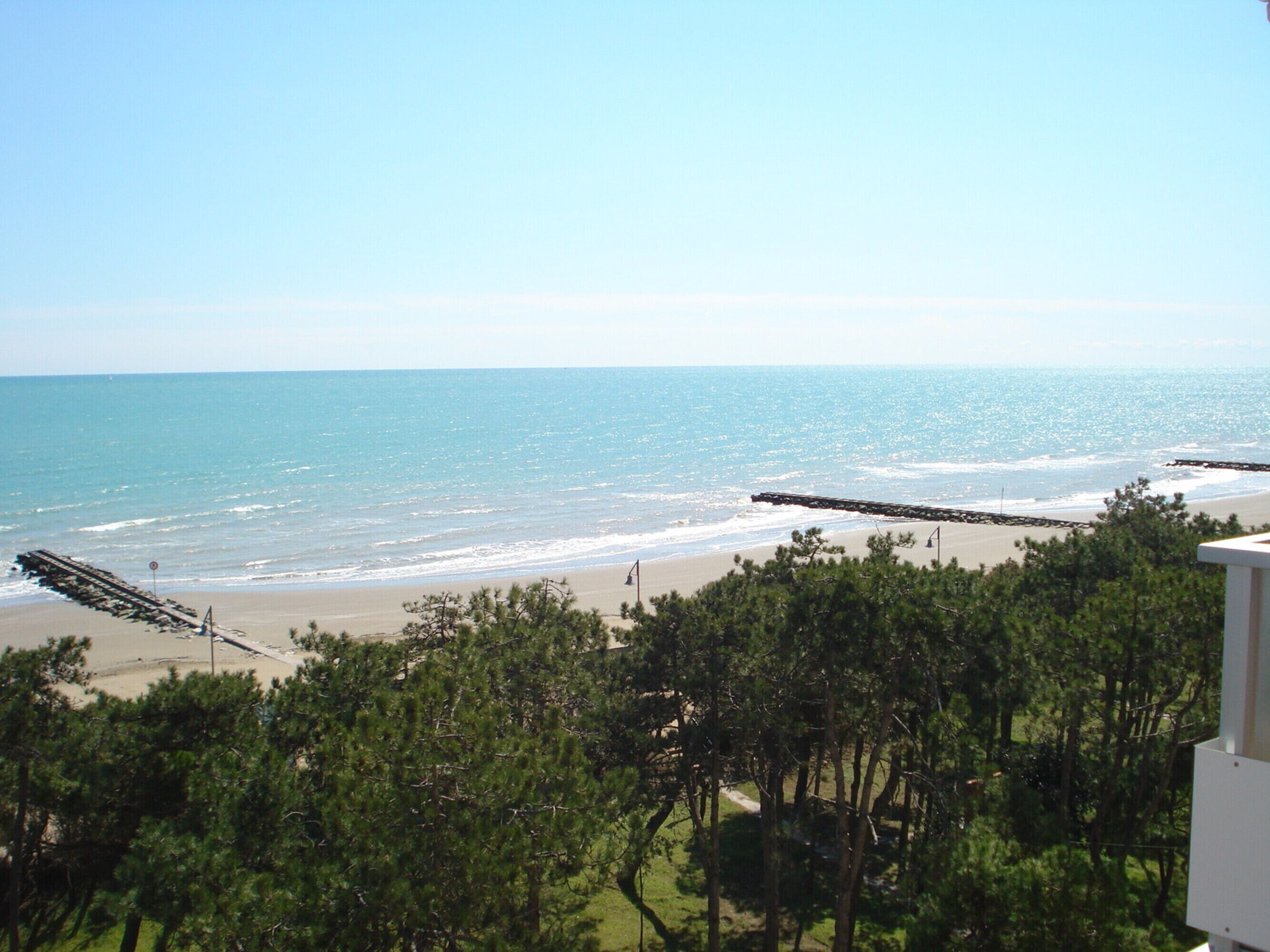 A beach with clear skies, a sandy shore, and a wooden pier extending into the water.