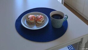 Une pièce avec une table blanche, une assiette remplie de nourriture, une tasse de café et une vue à travers une porte vitrée.
