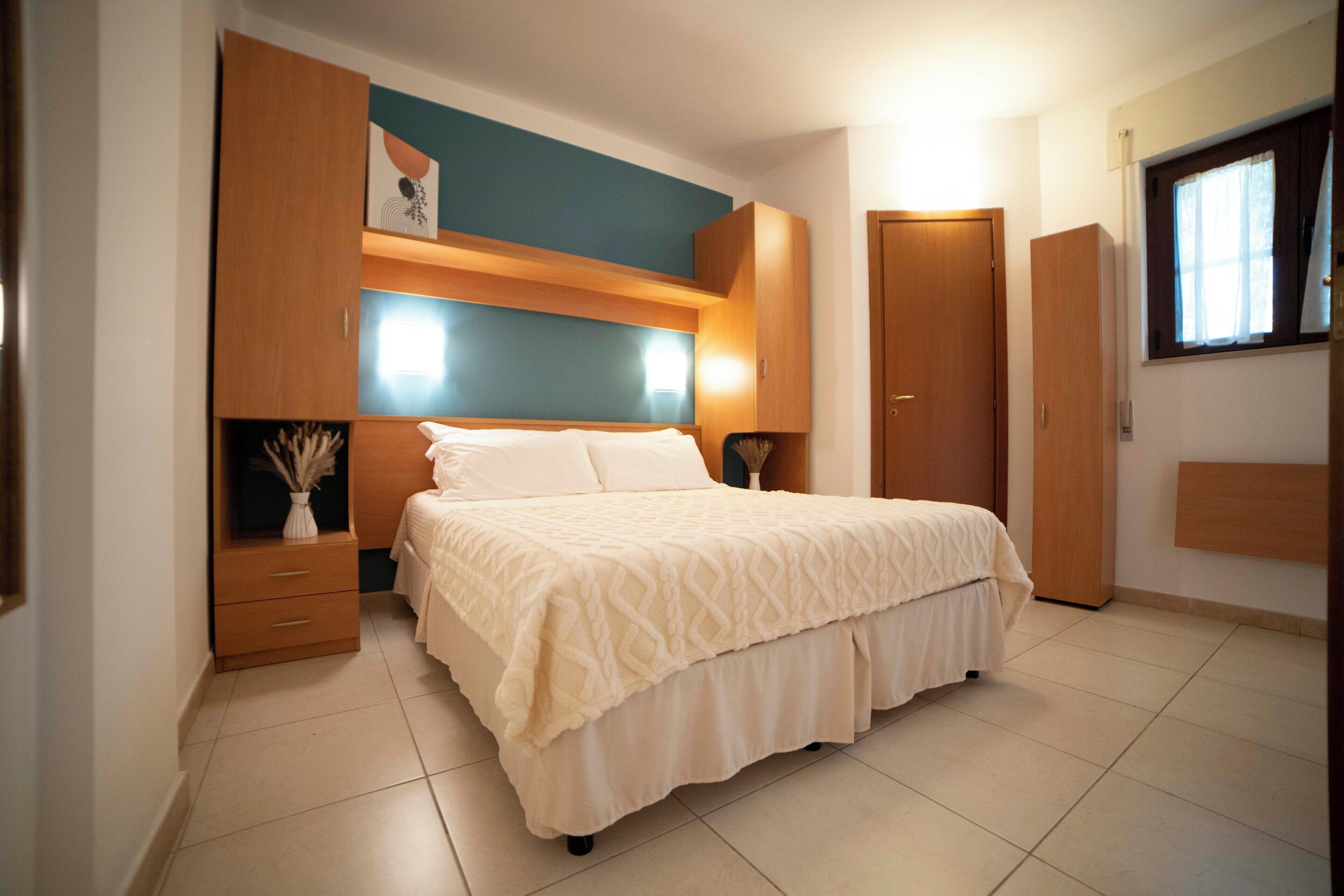 A bedroom with a bed, built-in wardrobe, bedside table, and a window with curtains.
