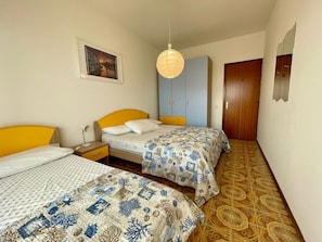 Quarto com duas camas, mesa de cabeceira, luminária pendente, guarda-roupa e porta.