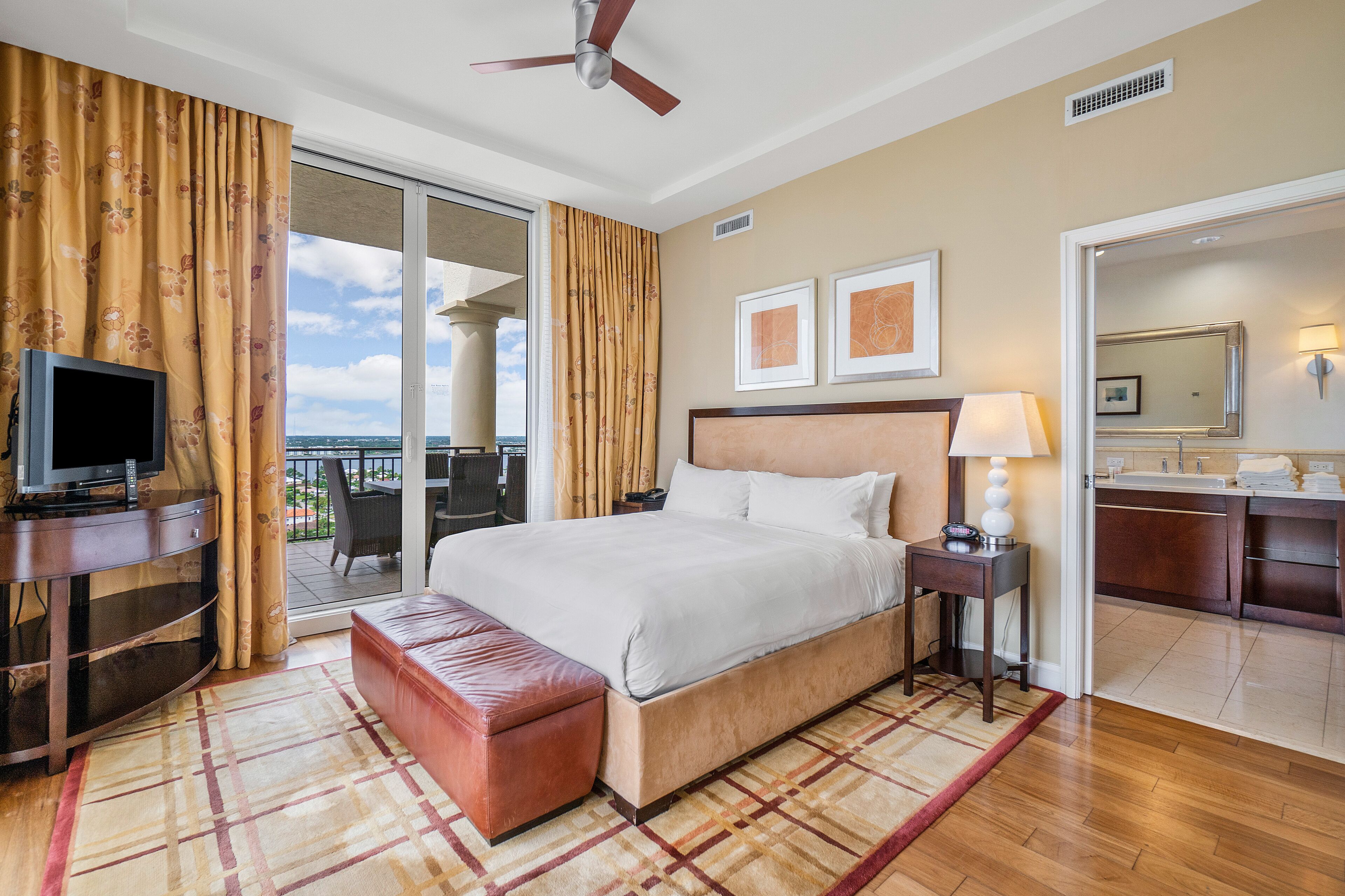 Ein Hotelzimmer mit Bett, Fernseher, Schreibtisch, Stuhl und einem Balkon mit Aussicht.