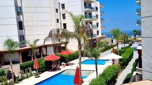A modern hotel with a swimming pool, red umbrellas, and palm trees. - Affordable Luxury by the Sea Porto Said (Al-Manasrah)