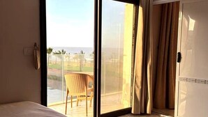 A hotel room with a large sliding glass door leading to a balcony with a view of the ocean and palm trees. - Affordable Luxury by the Sea Porto Said (Al-Manasrah)