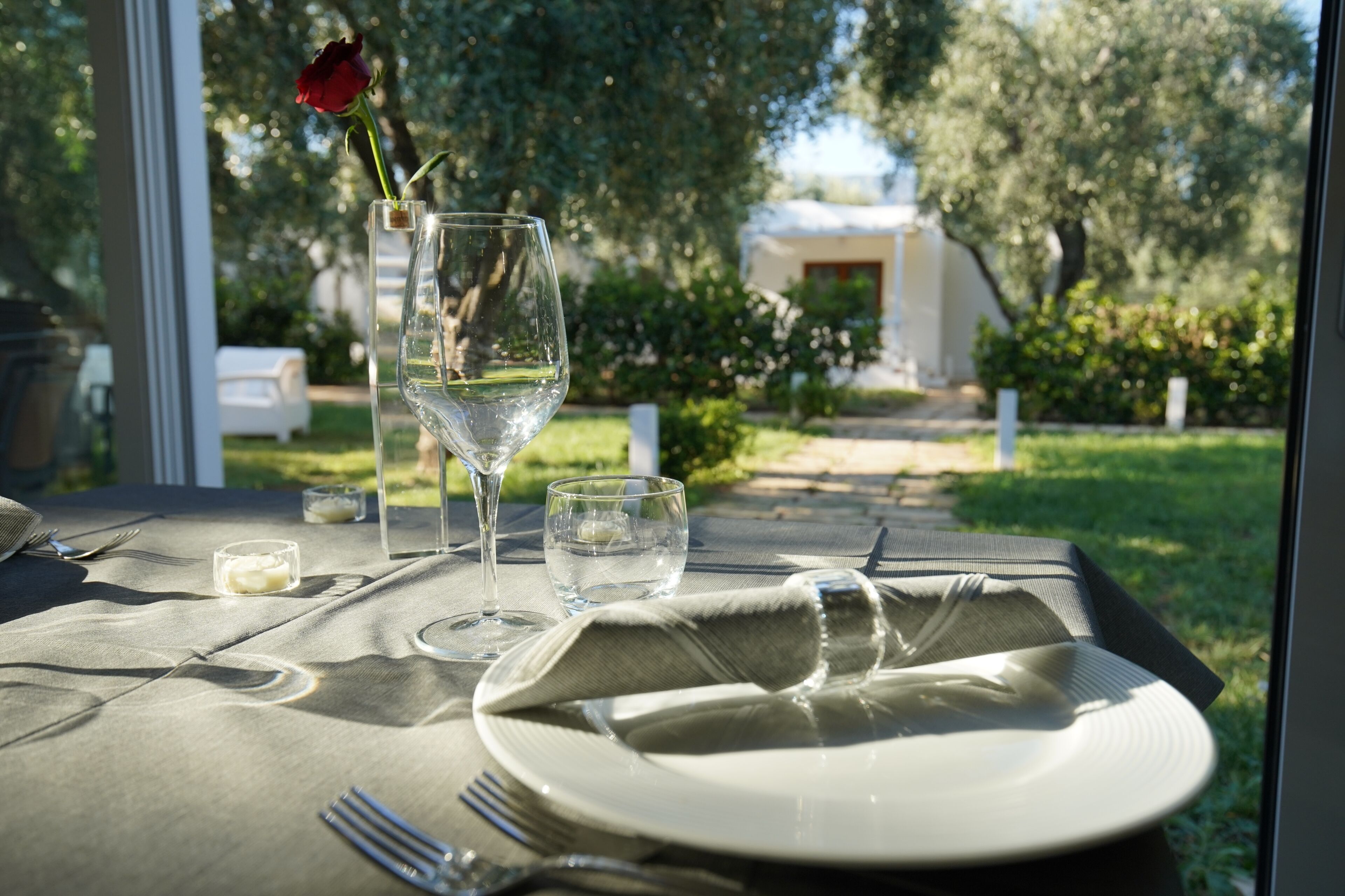 Une table dressée pour deux personnes, avec un verre de vin blanc, une rose et une bougie.