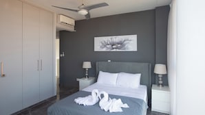 Habitación de hotel con una cama, dos mesitas de noche, ventilador de techo, equipo de aire acondicionado y un cuadro grande con motivos florales en la pared.