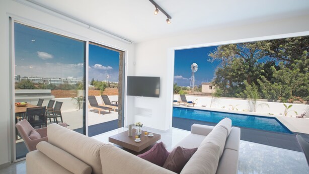A modern living room with a large window overlooking a swimming pool and a windmill. - Protaras Vie Bleu Villa Vb4 (Paralimni)