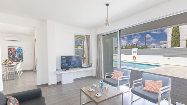 A modern living room with a pool view, a flat-screen TV, and a dining area. - Protaras Holiday Villa Ccv4 (Paralimni)