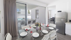 A dining area with a table set for six, a refrigerator, and a view of the outdoor pool. - Protaras Holiday Villa Ccv4 (Paralimni)