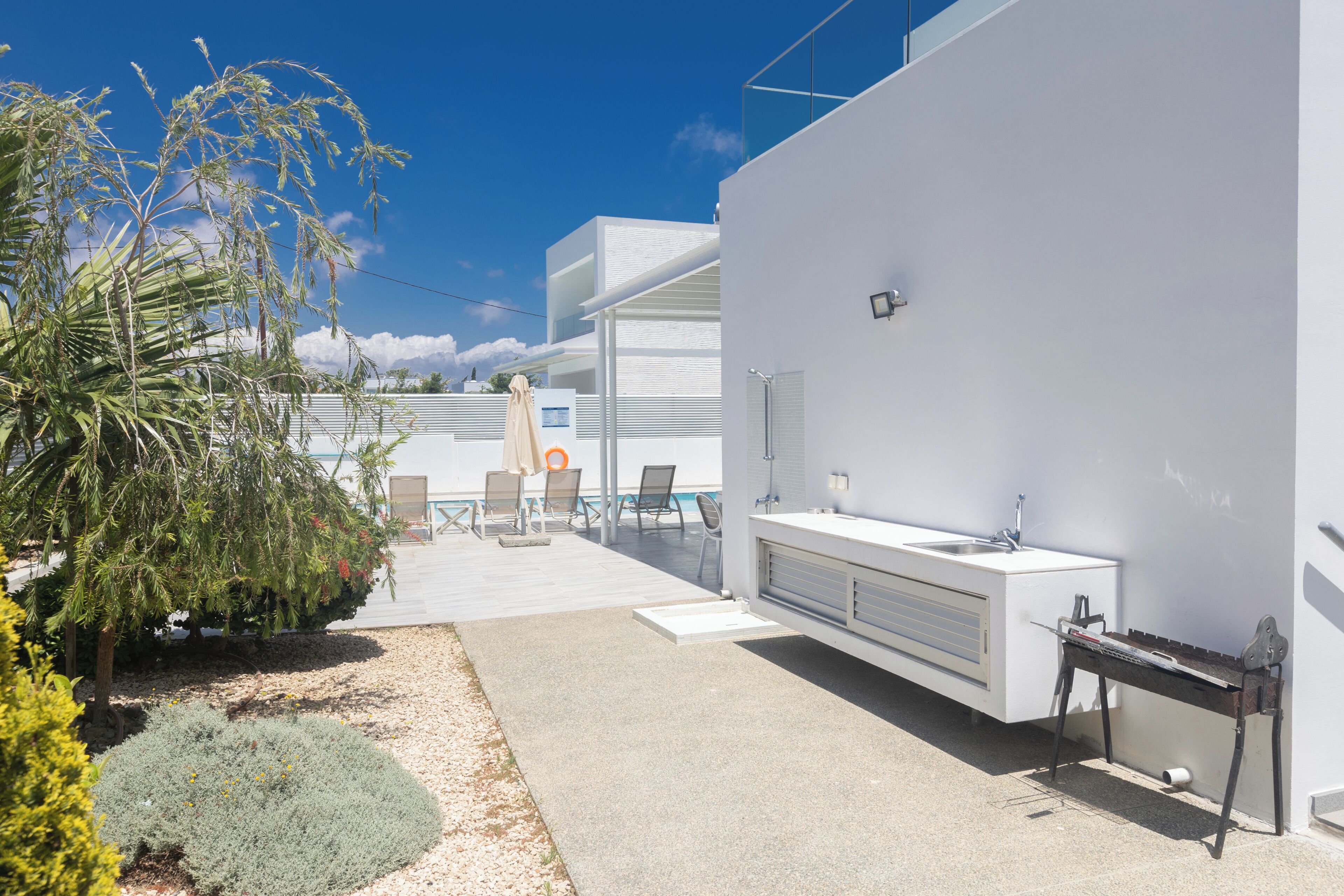 A modern outdoor kitchen area with a built-in sink and grill, surrounded by a patio with chairs and a small pool.