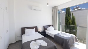 A hotel room with two beds, a balcony with a glass railing, and a view of trees. - Protaras Holiday Villa Ccv4 (Paralimni)