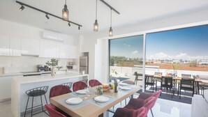 A modern kitchen with white cabinets, a dining area with red chairs, and a large window offering a city view. - 4 Bedroom Villa in Protaras Center - Protaras Vie Bleu Villa Vb3 (Paralimni)