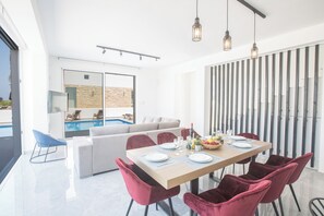 A modern dining area with a pool view, a sofa, and red chairs. - 4 Bedroom Villa in Protaras Center - Protaras Vie Bleu Villa Vb3 (Paralimni)