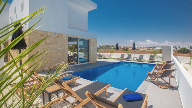 A modern outdoor pool area with lounge chairs and a clear view of the city skyline. - 4 Bedroom Villa in Protaras Center - Protaras Vie Bleu Villa Vb3 (Paralimni)