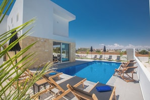 A modern outdoor pool area with lounge chairs and a clear view of the city skyline. - 4 Bedroom Villa in Protaras Center - Protaras Vie Bleu Villa Vb3 (Paralimni)